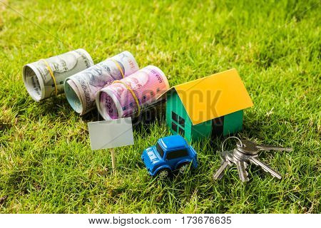 indian currency notes of rupees 100, 500 and 2000 in roll or stack with small home model, keys, toy car and calculator with blank board over green grass - home buying and finance concept in India