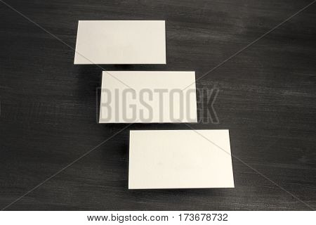 A photo of blank white thick cardboard business cards, floating above a dark wooden background texture. A mockup or a minimalist banner with copy space
