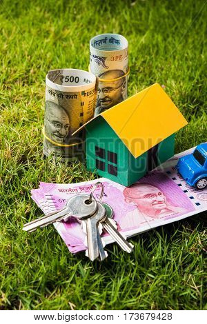 indian currency notes of rupees 100, 500 and 2000 in roll or stack with small home model, keys, toy car and calculator with blank board over green grass - home buying and finance concept in India