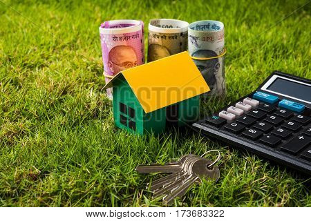 indian currency notes of rupees 100, 500 and 2000 in roll or stack with small home model, keys, toy car and calculator with blank board over green grass - home buying and finance concept in India