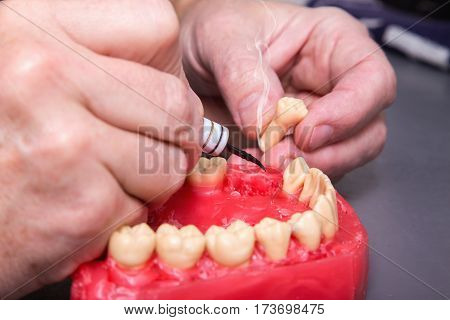 Close up of men's hands working with electric waxer on a red wax dental model on a grey table