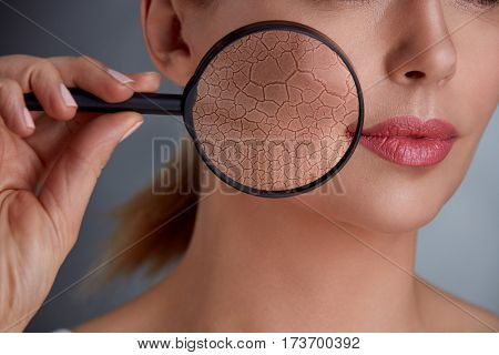 woman holding magnifier and showing damage to the skin, concept of rejuvenation and skincare