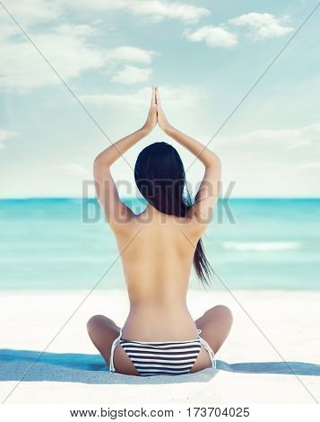 Young, beautiful girl with sexy body meditating on a beach without a bra. 