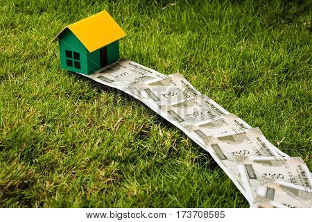 indian new currency notes of rupees 500 or 2000 forming a road to reach model house over green grass  - concept of residential property or home buying in india