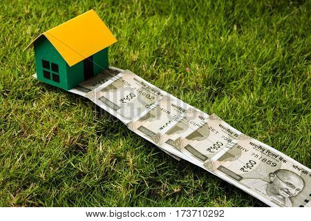 indian new currency notes of rupees 500 or 2000 forming a road to reach model house over green grass  - concept of residential property or home buying in india