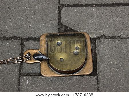 Small statue of mouse which eating cheese on paving stones .