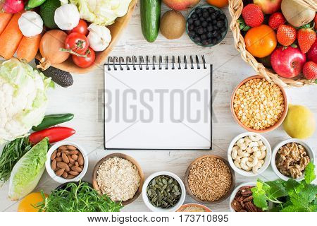 Variety of fruits and vegetables cereals nuts on the white wooden table top view copy space for text selecitve focus. Basket of strawberries apples oranges kiwi bowls of oats spelt rice kamut peas; broccoli cauliflower garlic tomatoes peppers