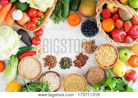Variety of fruits and vegetables cereals nuts on the white wooden table top view copy space for text selecitve focus. Basket of strawberries apples oranges kiwi bowls of oats spelt rice kamut peas; broccoli cauliflower garlic tomatoes peppers