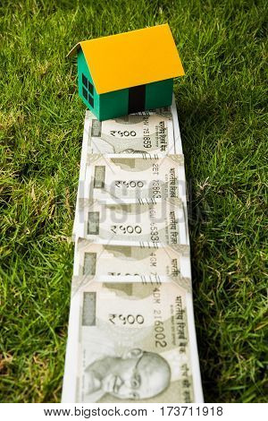 indian new currency notes of rupees 500 or 2000 forming a road to reach model house over green grass  - concept of residential property or home buying in india
