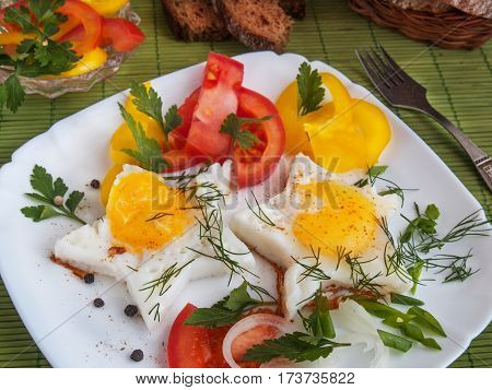 Fried eggs in the form of star shape fried in butter with vegetables peppers tomatoes parsley dill onions on a white porcelain plate with bread