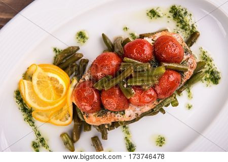 Grilled trout with tomatos leguminous beans and lemon on white plate. Top view