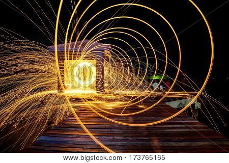 Hot Golden Sparks Flying from Man Spinning Burning Steel Wool on Wooden Bridge Extended into the Sea. Long Exposure Photography using Steel Wool Burning.