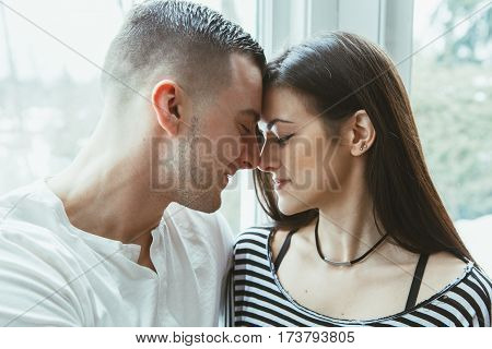 Portrait of beautiful romantic young couple man woman in love hugging kissing indoors at home toned with filters authentic lifestyle