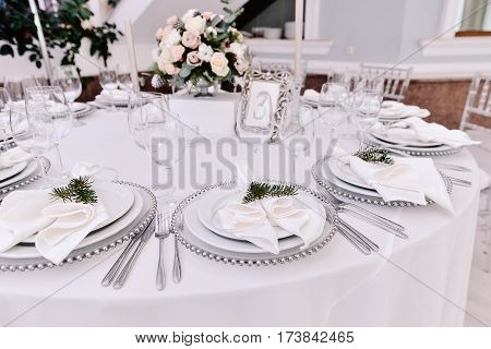 Well decorated guest numbered table in tenderless wedding hall, which is in white and silver colours