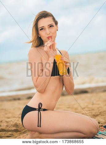 Beach woman drinking cold drink beverage having fun at beach party. Female babe in bikini enjoying orange water from glass boutle. summer concept
