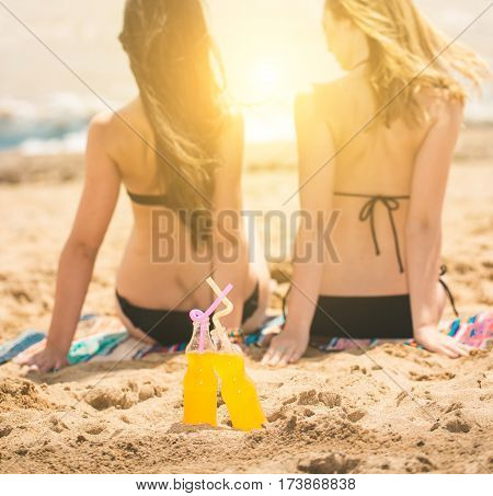Gierlfriends drinking cold drink beverage having fun at beach party. Female babes in bikini enjoying orange water from glass boutle. summer concept