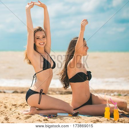 Gierlfriends drinking cold drink beverage having fun at beach party. Female babes in bikini enjoying orange water from glass boutle. summer concept