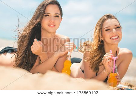 Gierlfriends drinking cold drink beverage having fun at beach party. Female babes in bikini enjoying orange water from glass boutle. summer concept