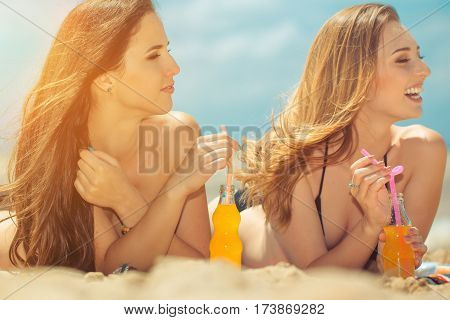Gierlfriends drinking cold drink beverage having fun at beach party. Female babes in bikini enjoying orange water from glass boutle. summer concept