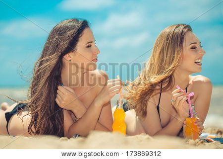Gierlfriends drinking cold drink beverage having fun at beach party. Female babes in bikini enjoying orange water from glass boutle. summer concept