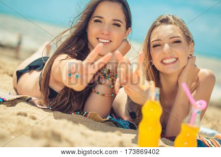 Gierlfriends drinking cold drink beverage having fun at beach party. Female babes in bikini enjoying orange water from glass boutle. summer concept