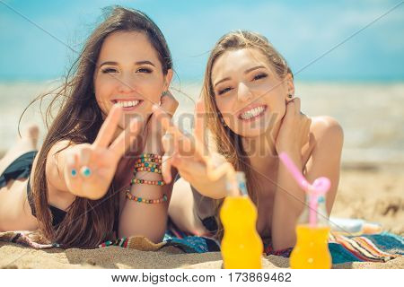 Gierlfriends drinking cold drink beverage having fun at beach party. Female babes in bikini enjoying orange water from glass boutle. summer concept