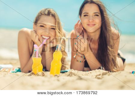 Gierlfriends drinking cold drink beverage having fun at beach party. Female babes in bikini enjoying orange water from glass boutle. summer concept