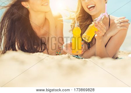 Gierlfriends drinking cold drink beverage having fun at beach party. Female babes in bikini enjoying orange water from glass boutle. summer concept