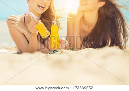 Gierlfriends drinking cold drink beverage having fun at beach party. Female babes in bikini enjoying orange water from glass boutle. summer concept