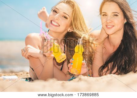 Gierlfriends drinking cold drink beverage having fun at beach party. Female babes in bikini enjoying orange water from glass boutle. summer concept