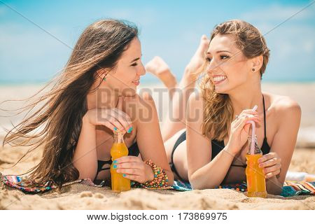 Gierlfriends drinking cold drink beverage having fun at beach party. Female babes in bikini enjoying orange water from glass boutle. summer concept