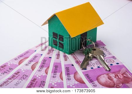 indian real estate or residential model house with new currency notes, keys, toy car and calculator, selective focus