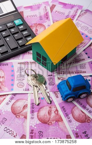 indian real estate or residential model house with new currency notes, keys, toy car and calculator, selective focus