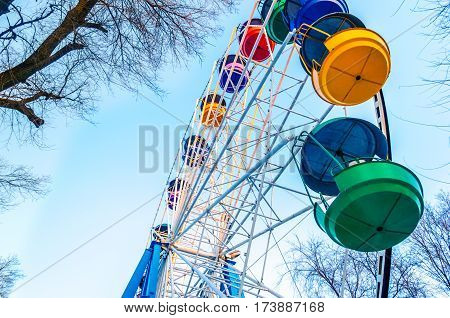 old Ferris wheel with colored cabins open against the blue sky