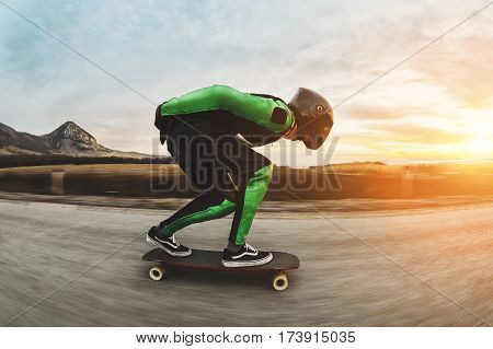 A young man in a fullface helmet and a leather suit in a special rack rides a longboard on afsaltu sunset in the background mountains and beautiful sky at high speed.