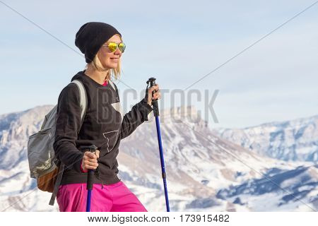 Young beautiful girl in sunglasses with Nordic poles in the sunset light on the background of the Caucasian ridge and rock