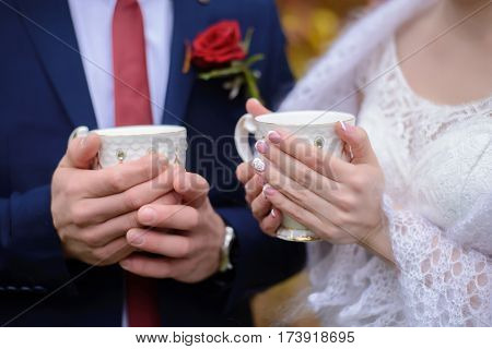The bride and groom are holding white mugs of hot tea to warm up