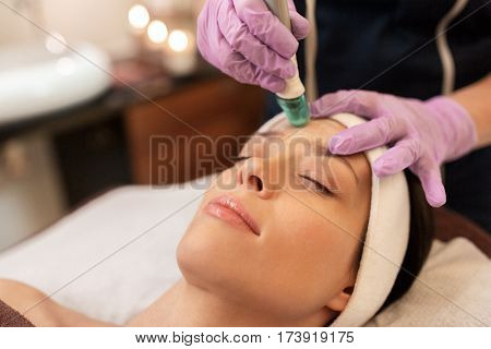 people, beauty, cosmetology, exfoliation and technology concept - beautiful young woman having microdermabrasion facial treatment with crystals in spa