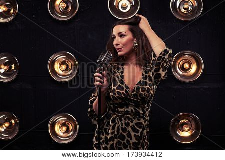 Full-length shot of stunning woman in chiffon leopard dress. Standing in studio and looking at camera. Loose Curly Hair. Pretty girl with evening makeup in eveningwear
