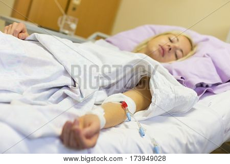 Bedridden female patient lying in hospital bed, receive infusion while recovering after surgery.