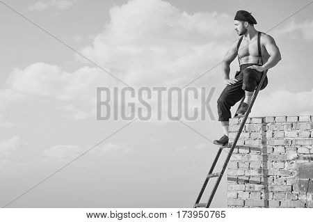 The best worker. Relaxed handsome muscular shirtless handyman sitting on top of the ladder at construction object copyspace monochrome black and white confidence masculinity building industry concept