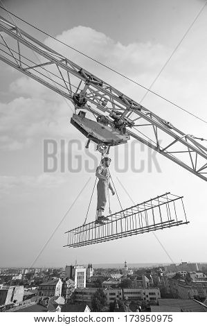 Alone up here. Low angle monochrome shot of a builder standing on a crossbar working on a construction site city urban development business engineer professional fearless masculinity worker concept