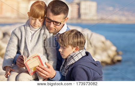 Father reading a book to his children outdoors