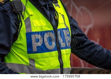 Close up of Swedish police officer wearing a luminous yellow green vest with police text.