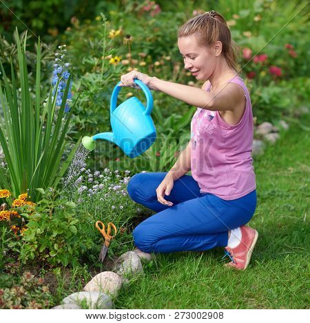 Smiling Caucasian Woman Watering Flowers With Water Can On A Croft.