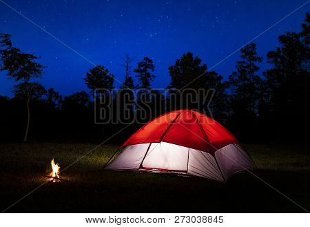 Stars And A Small Campfire With A Lighted Tent In A Field
