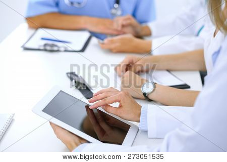 Doctor Using Tablet Computer At Medical Meeting, Closeup. Group Of Colleagues At The Background