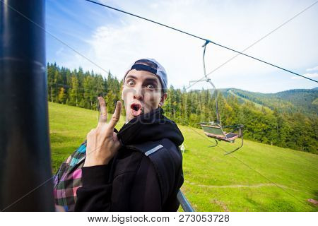 Man With Funny Face Sitting On The Chairlift During Summer Hike In Mountains