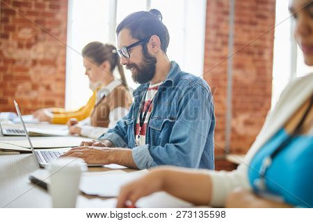 Young casual businessman sitting in front of lapto pand concentrating on web design work