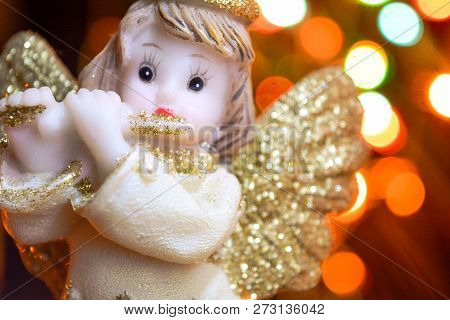 Figurine Of Little Angel With Golden Shiny Wings And Halo That Plays Flute On Shining Background Of 